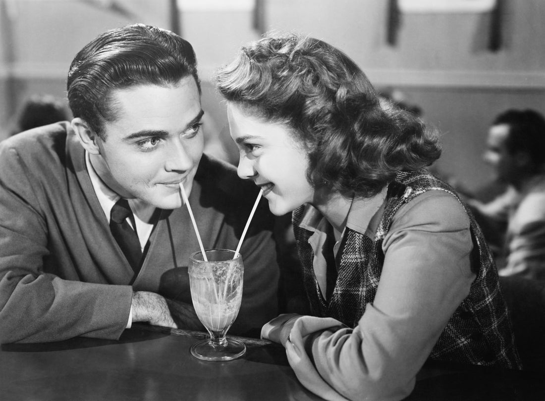 Retro photo of couple sharing a milkshake. Blog highlights ways to express love through Gift Giving.