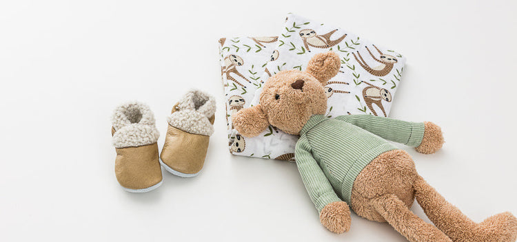 Gifts displayed out of gift box include soft toy, swaddle, leather shoes.