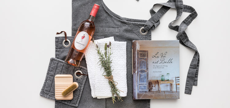 Products featured out of gift box. Sauce for BBQ, kitchen dish cloth and towel, tampico dish brush, candle, seasoning, acacia wooden board, chocolate and wine.
