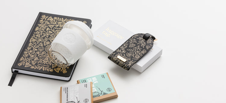 Journal and boxed luggage tag, hand blown SOL reusable cup and chocolate. Flatlay of products featured outside of gift box.