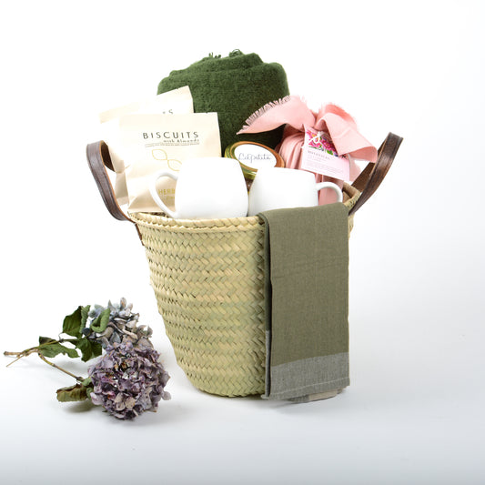 Cozy gift basket with throw blanket, ceramic mugs, hot chocolate, candle, tea towel, and almond biscuits. A luxury comfort gift NZ