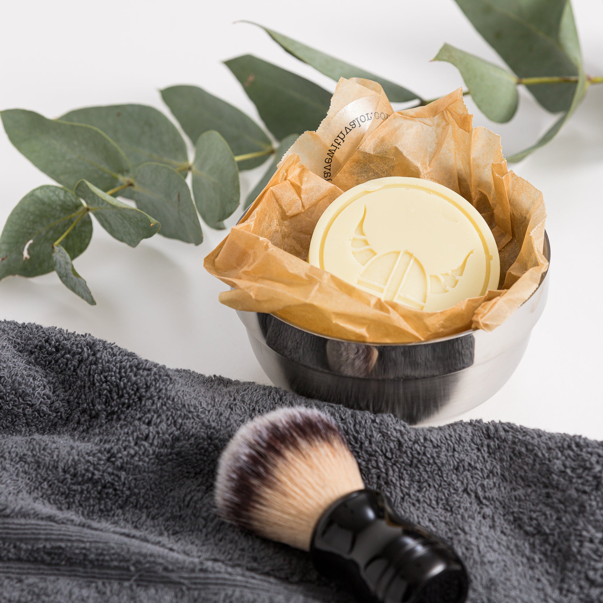 Close up of products out of gift box are shaving dish and soap, brush and towel.