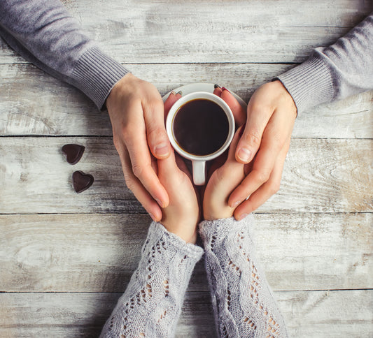 Two people holding hands over a cup of coffee to show how Gift Giving connects us.