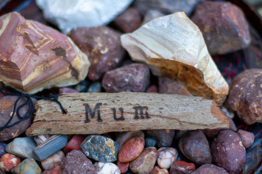Engraved piece of wood on pebbles at beach. Blog highlights gifts for mums.