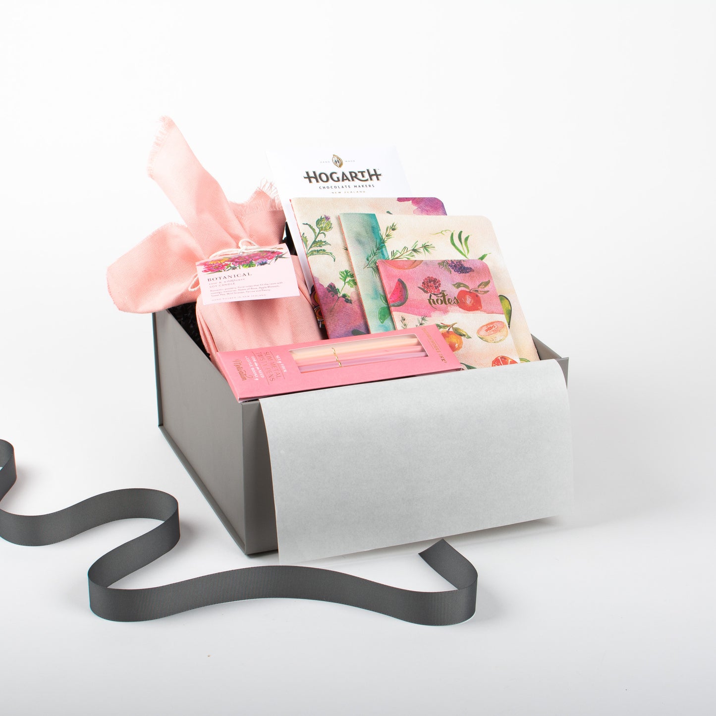 A gift box containing a variety of items including a notebook, a candle, a pen, and some chocolate, all beautifully presented.
