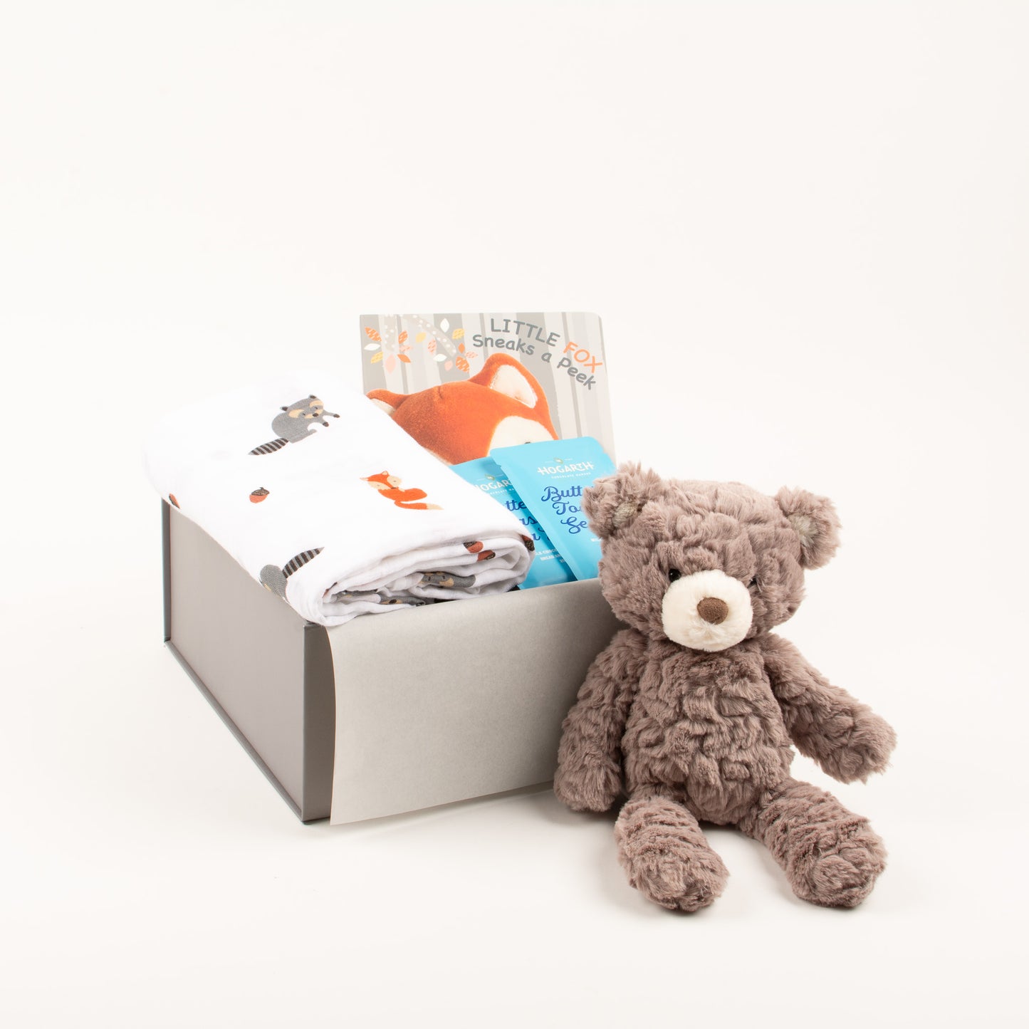 Soft swaddle, soft toy, book and chocolate displayed next to gift box.