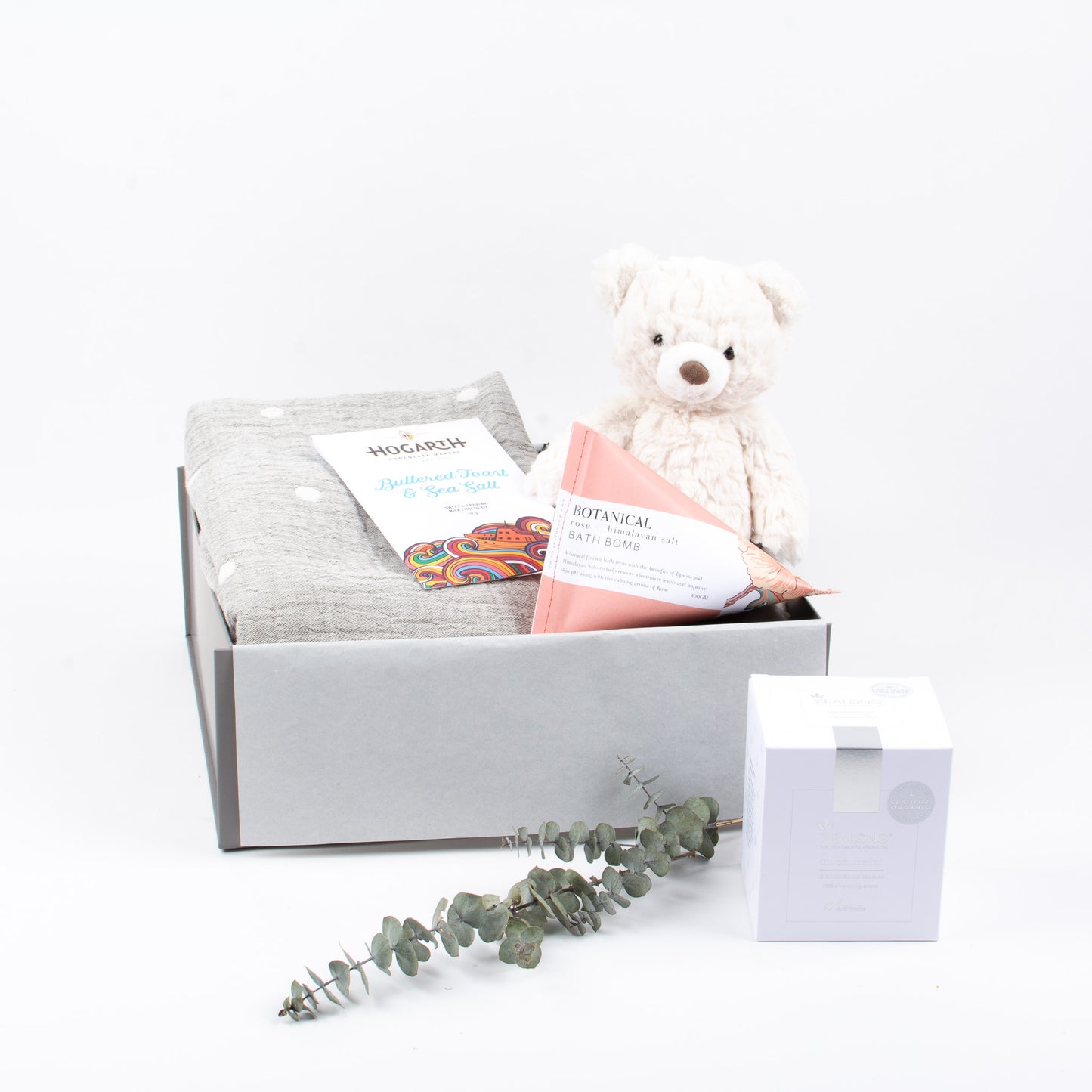 Luxury blanket, chocolate, herbal tea, bath bomb and sot toy displayed in gift box.