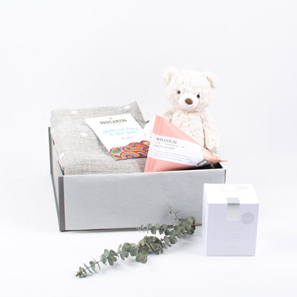 Luxury blanket, chocolate, herbal tea, bath bomb and sot toy displayed in gift box.