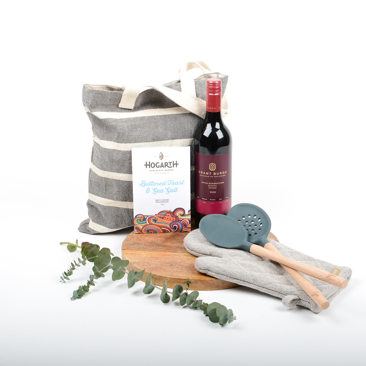 Wine bottle, tote bag, wooden serving board, slotted spoon, and oven glove on a white background