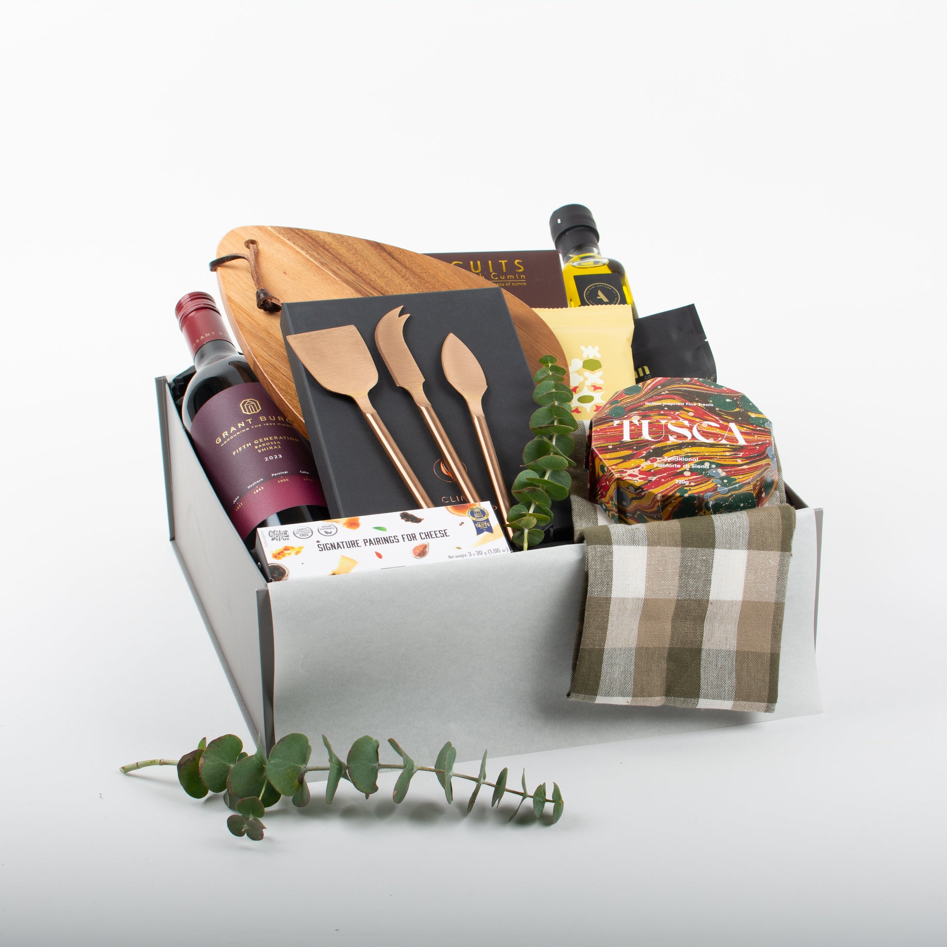A gift box containing a variety of gourmet food items and a cheese board with utensils, wine, and savoury biscuits.