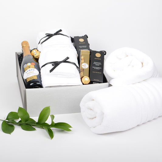 Gift basket with white towels, a bottle of non alcohol bubbles and other items on a white background