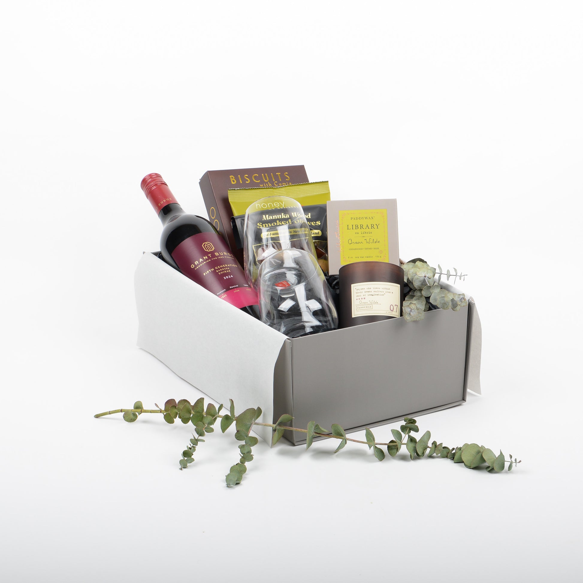 Open gift box with wine, 2 stemless glasses, treats and olives and scented candle.