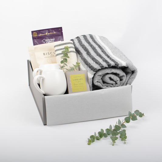 A gift box with throw, candle, mugs, chocolate drink and biscuits.