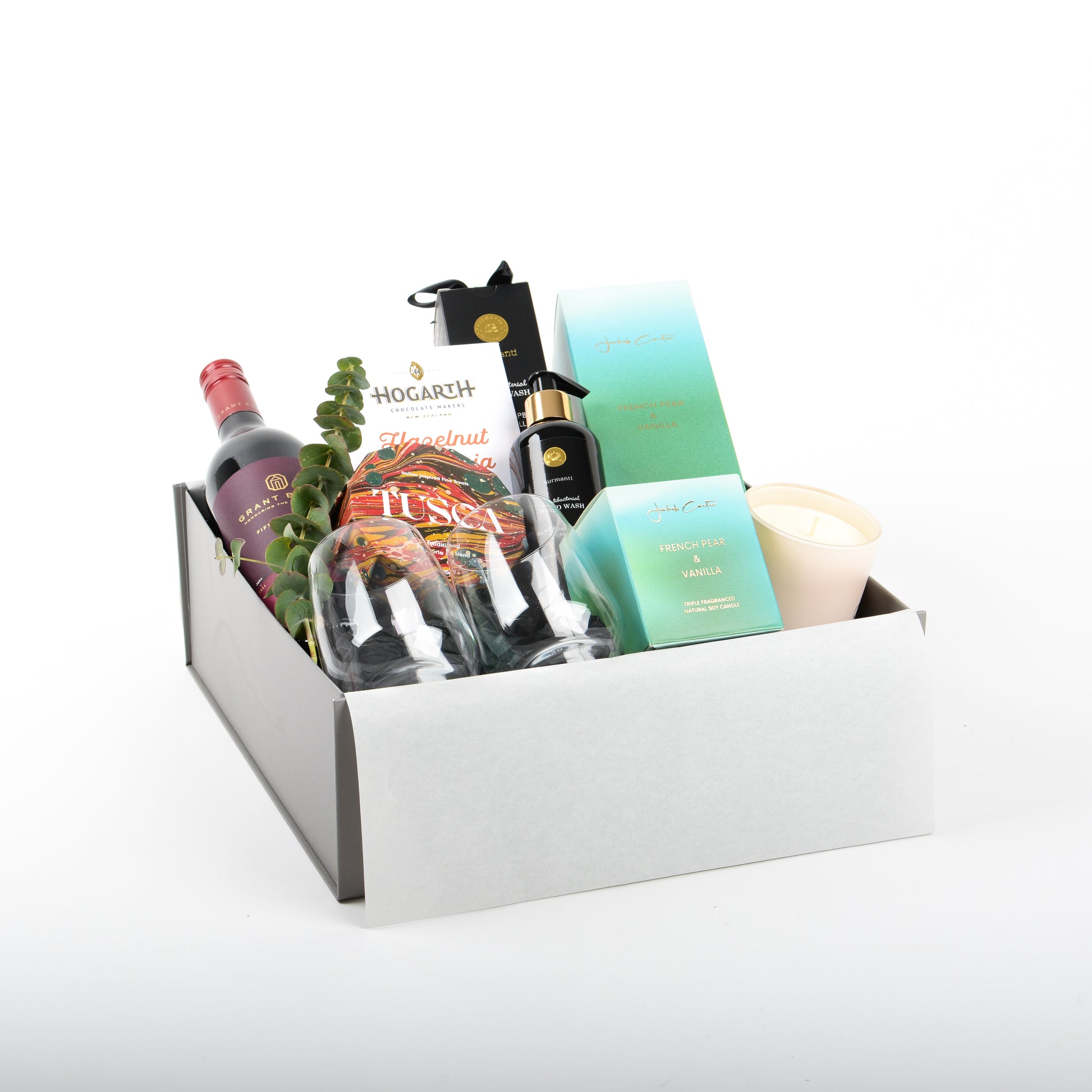 A gift box featuring red wine, wine tumblers, panforte, reed diffuser, and candle, a luxury new home gift NZ