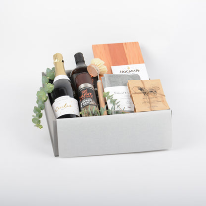 Gift box with artisan cheese board, sauce, grinder, kitchen ware, bubbles and seasoning.