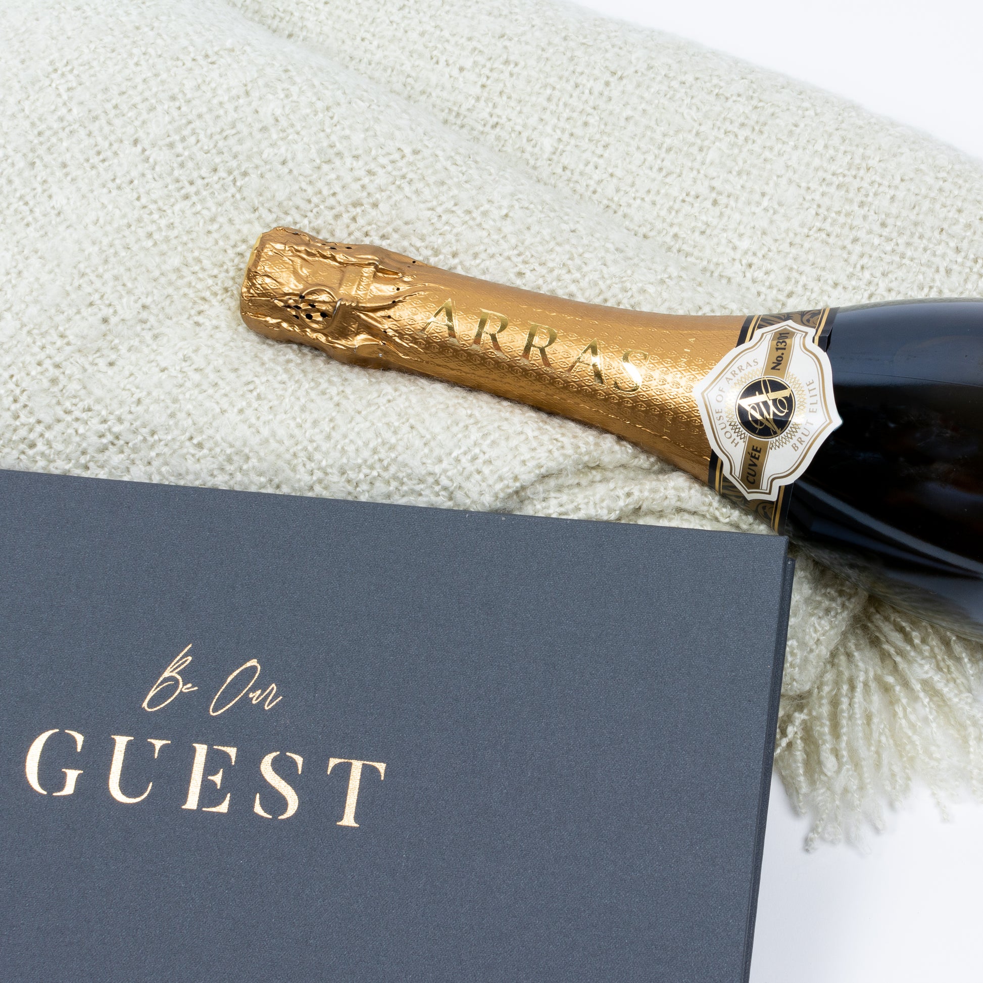Out of gift box close up of brut cuvee, guest book, cosy throw.