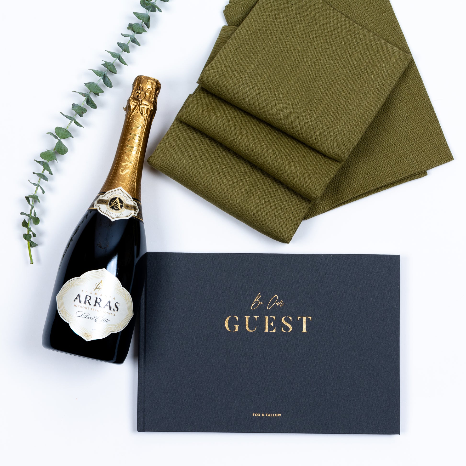 Products featured out of gift box are linen napkins, guest book, bubbly. 