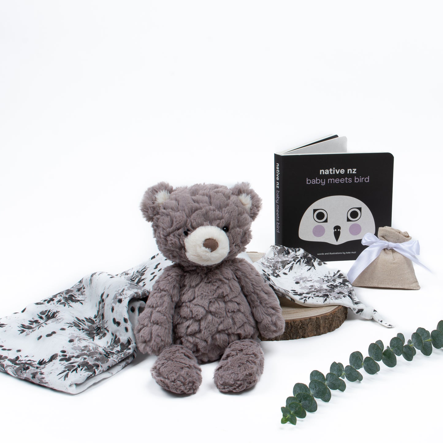 Flatlay of products out of gift box are swaddle and knot hat, soft toy, book, lavender pouch.