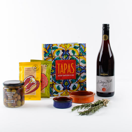 Products displayed out of gift box are red wine, book, spices, olives, tapas dishes.