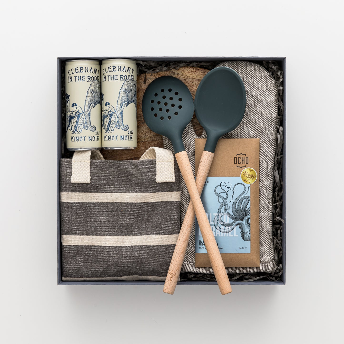 Gift box includes wooden board, two red wine cans, slotted spoon, spoon, tote bag, oven mitt, chocolate.