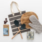 Products shown out of gift box are wooden board, spoon, slotted spoon, oven mitt, red wine in cans, chocolate, tote bag.