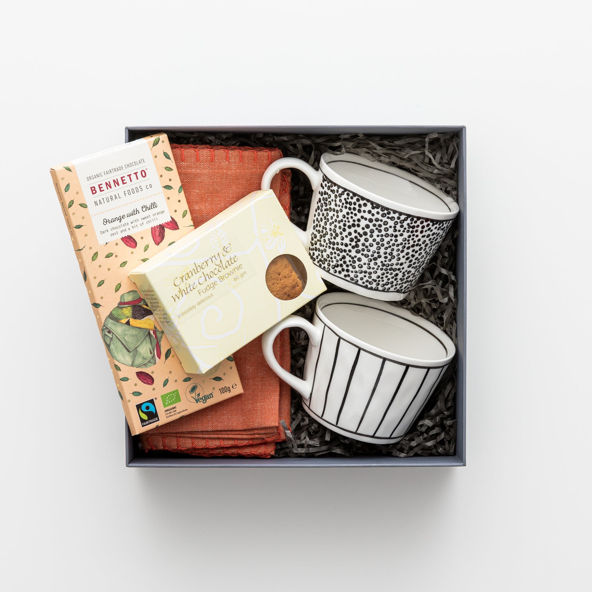 Gift box contains two mugs, two napkins, chocolate, brownie.