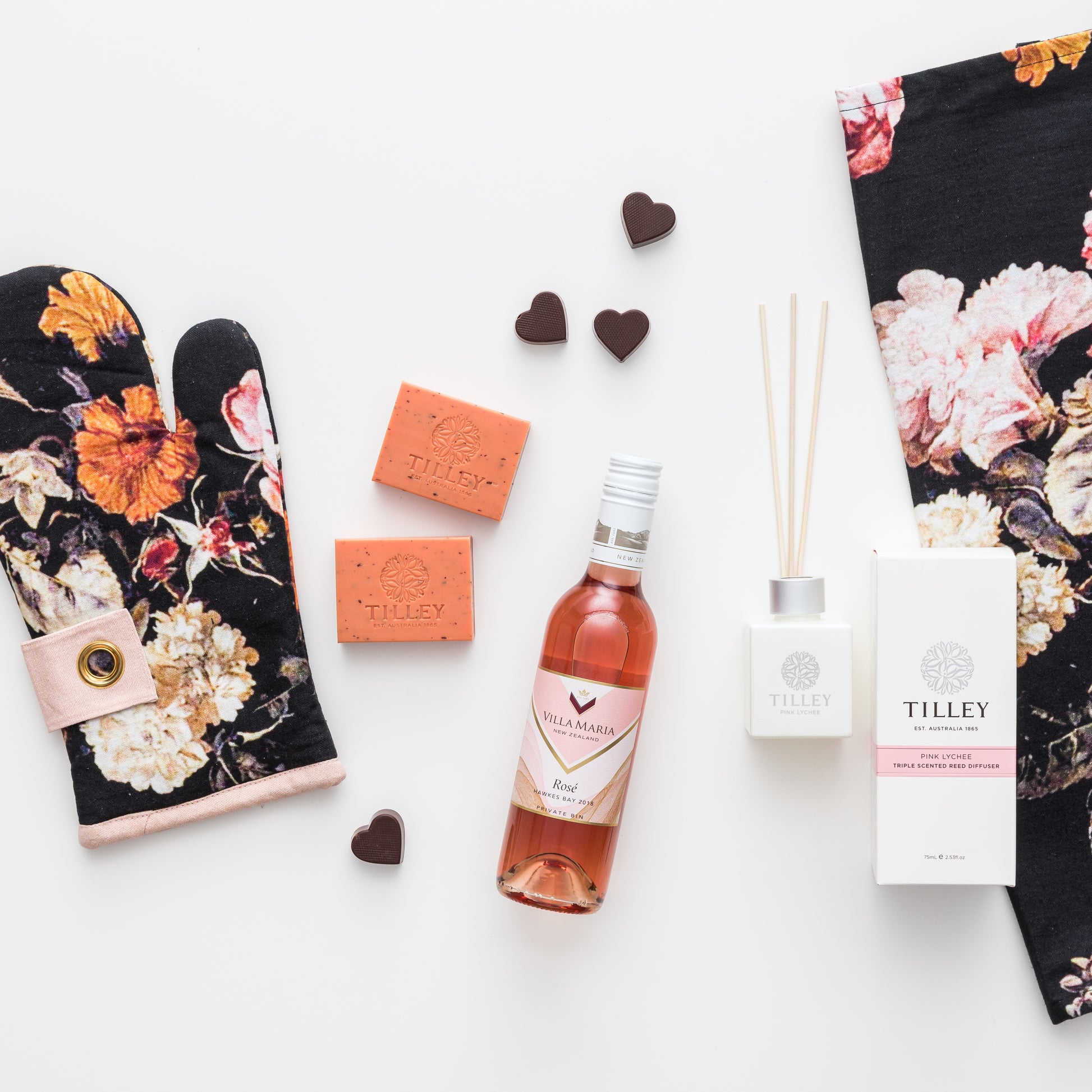 Products featured out of gift box are rose wine, chocolate, reed diffuser, oven mitt, tea towel, soap.