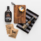 Featured products shown out of gift box are tea towel, bourbon sauce, pepper grinder, seasoning, salt, wooden board.