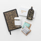 Products featured out of gift box are journal, luggage tag, reusable cup, chocolate.