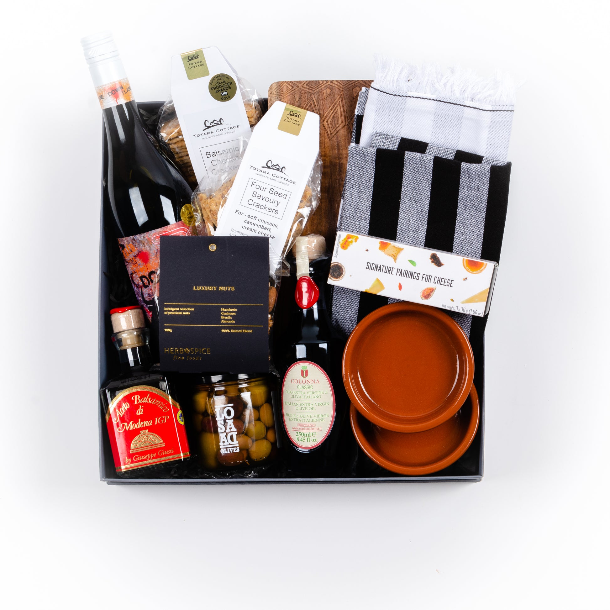Gift box includes wooden board, two tea towels, two tapas dishes, two crackers, nuts, cheese jellies, olives, olive oil, balsamic vinegar, red wine.