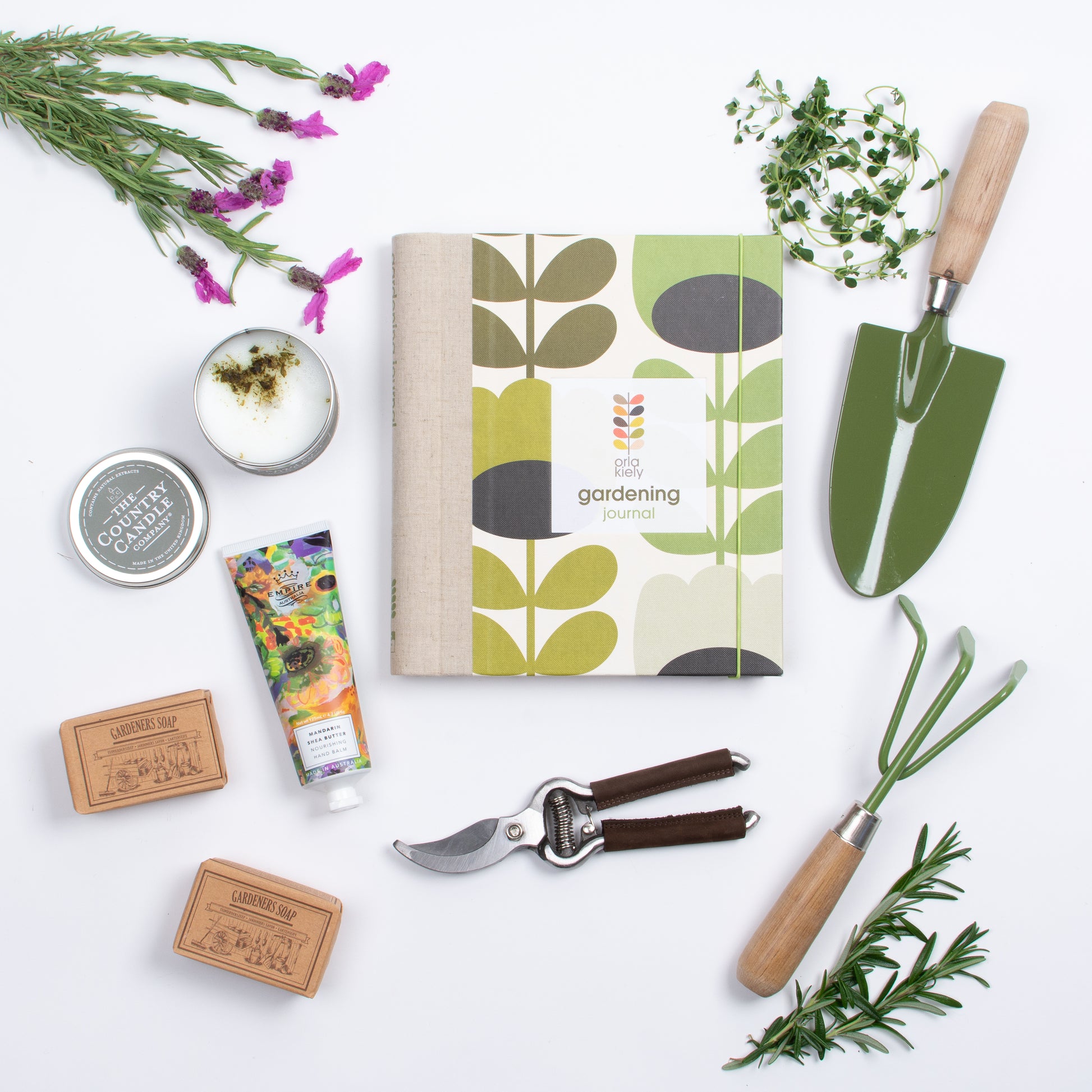 Flatlay of products are book, gardening fork and spade, two soaps, candle, hand cream, pruner.