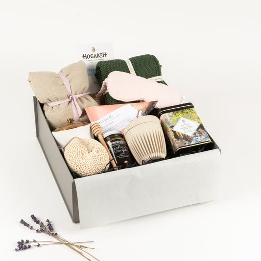 Wellness Deluxe - Gift Boxes NZ - Gifts of Distinction.  This gift box features a linen heat pillow, eye mask, cotton hand towel, craft chocolate by Hogarth, Hygge candle, cotton loofah, botanical bath bomb, herbal tea, reusable Huskee cup, artisan honey and dipper.