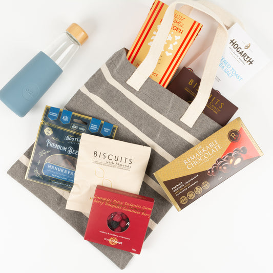 Treat Bag Elite - Gift Boxes NZ - Gifts of Distinction.  This gift box is filled with treats, canvas tote bag,caramel popcorn, biscuits, craft chocolate by Hogarth, scorched almonds, jerky, gummies, almond biscuits and handblown reusable drink bottle by SOL.
